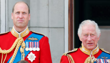 Prince William and King Charles wear red military uniforms as they stand on the Buckingham Palace balcony