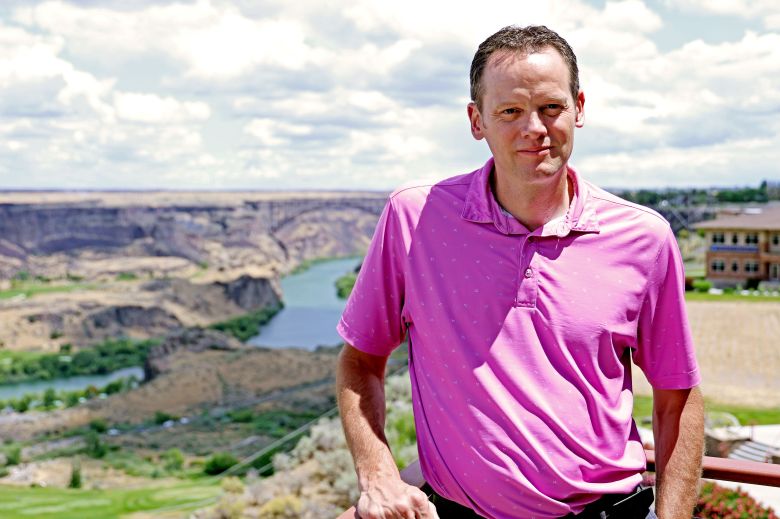 Person in a pink polo shirt standing in front of a river and canyon landscape.