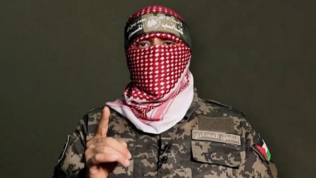 Abu Obeida, Hamas military spokesman, appears in military uniform with a red keffiyeh covering his face during a televised statement.