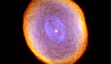 Planetary nebula IC 418 appears as a cloudy oval with intricate patterns. The outer edge is reddish, and the rest of it is light purple. There is a light red central star.