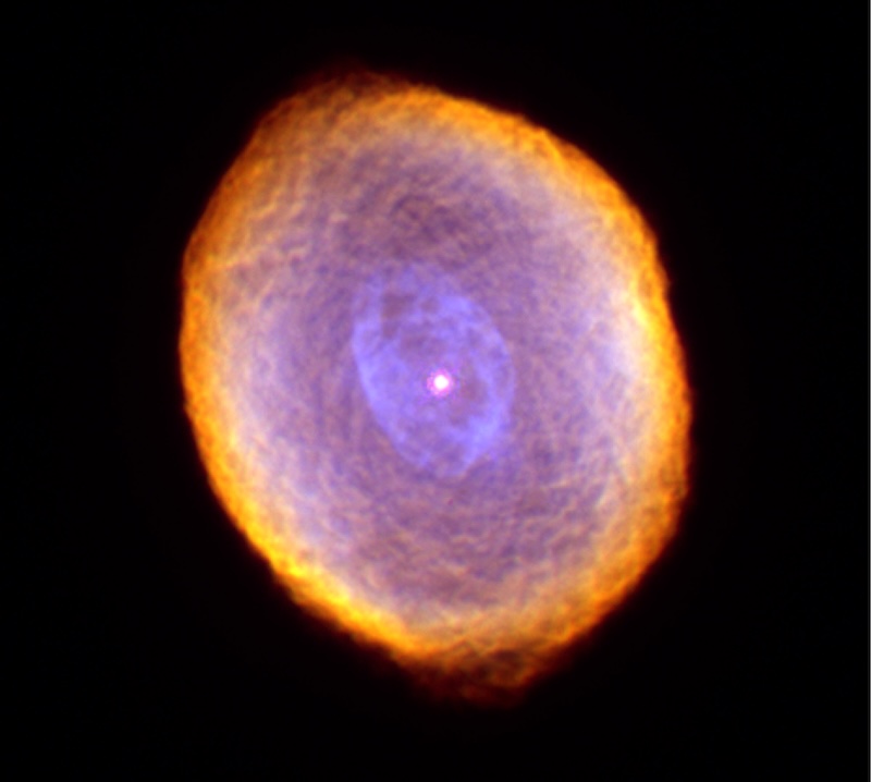Planetary nebula IC 418 appears as a cloudy oval with intricate patterns. The outer edge is reddish, and the rest of it is light purple. There is a light red central star.