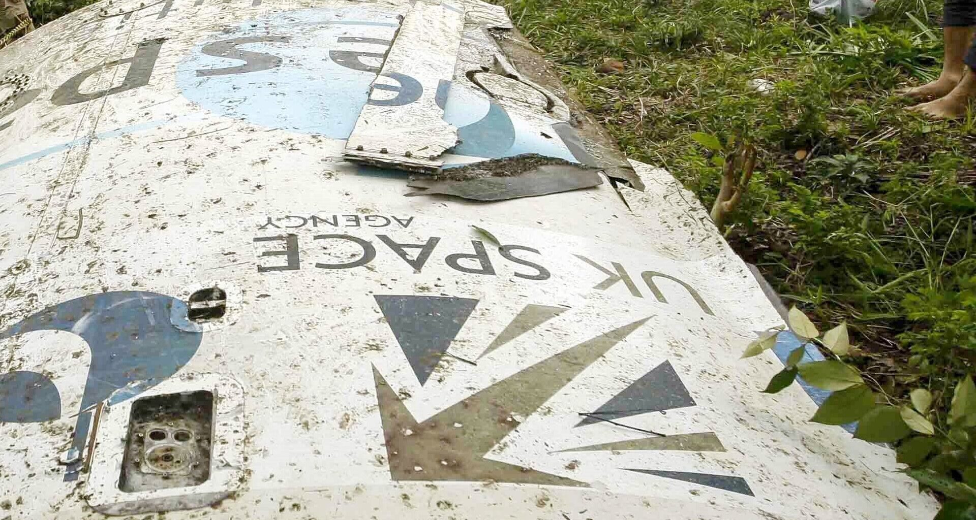 A white metal piece of space debris lies on a grassy lawn with the words &quot;UK Space&quot; upside down with the logo.