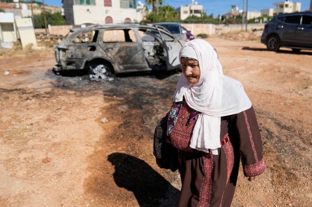 A woman walks past a vehicle that was burnt overnight by Israeli settlers