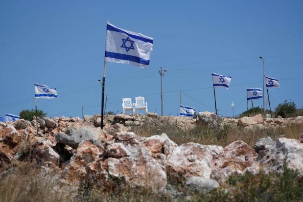 Israeli flags flutter on top of a hill that is adjacent to Palestinian properties