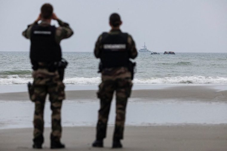 French Gendarme observe migrants onboard a smuggler's boat as they sail in an attempt to cross the English Channel off the beach of Hardelot in Neufchatel-Hardelot, northern France on August 13, 2025. One week after it came into force, the Franco-British migration agreement is causing turmoil among asylum seekers flocking to the northern coast of France, but has not yet stopped illegal crossings of the English Channel. (Photo by Sameer Al-DOUMY / AFP) (Photo by SAMEER AL-DOUMY/AFP via Getty Images)