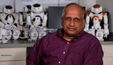 Sam Thangiah sitting in the Robotics Lab at SRU in front of humanoid robots.