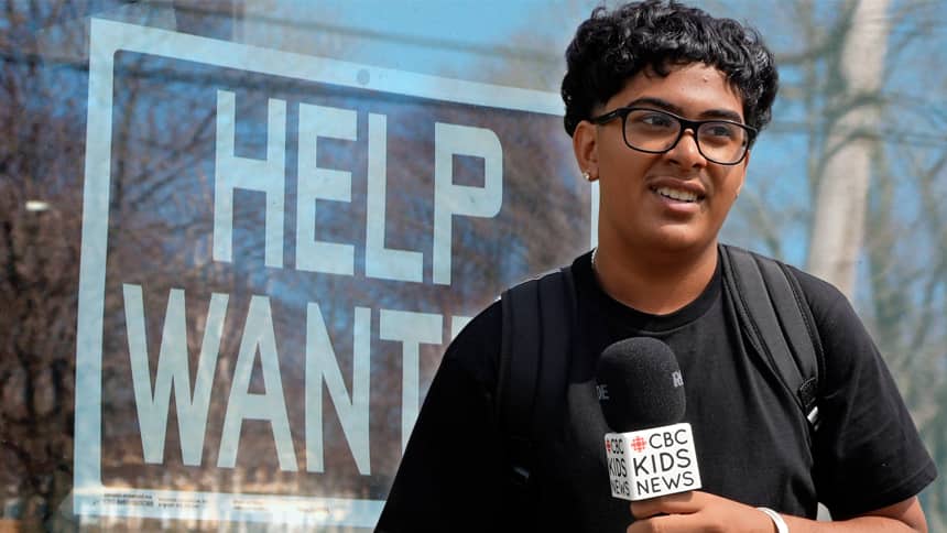 A teen boy in a black shirt with glasses holds a CBC Kids News microphone. Behind him is a help wanted poster.