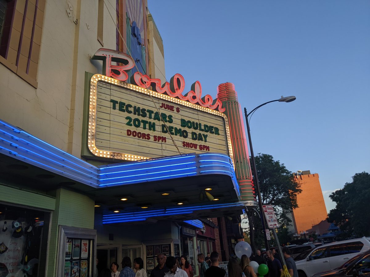 The marquee of a venue displays information for "Techstars' Last Demo Day in Boulder," celebrating the 20th event with time details. People are gathered outside under a partly cloudy sky.