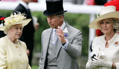 Queen Elizabeth II wears a pale yellow outfit while her son King Charles waves in front of her face, and Queen Camilla stands to the side ignored wearing white