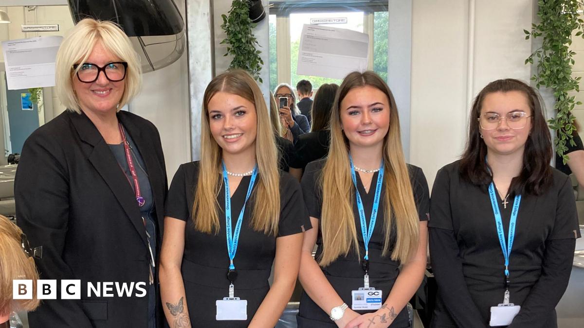 Three young girls standing next to their female college tutor. The tutor has short blonde hair and is wearing glasses with thick black frames. The two girls to her left have long blonde hair. The girl on the end of the line has long dark hair. All of them are wearing black and have lanyards around their necks.