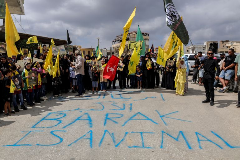 Protestors hold up Hezbollah flags behind graffiti reading "Barak is animal", as they demonstrate against the planned visit of US envoy Tom Barrack to south Lebanon, on August 27, 2025, in Khiam.
