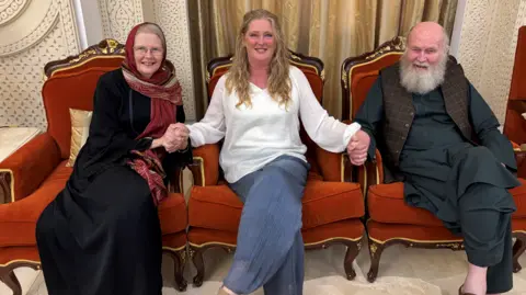 Family handout Freed British couple peter and barbie Reynolds sit with their daughter sarah. On the left, Barbie is wearing a dark dress. A blond haired Sarah is sat in the middle of the two, wearing blue jeans and a white top. On the right sits Peter, he's wearing a traditional Afghan dark top and trousers, with a brown textured waistcoat. All are smiling at the camera.