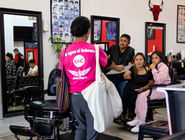 Dolores Castañeda distributes flyers in a Little Village barbershop on Aug. 31, 2025, to alert residents of the potential immigration raids and how they can protect themselves. (Brian Cassella/Chicago Tribune)