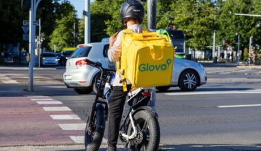 Poznan, Polonia - 30 iunie 2025: Curierul Glovo, cu rucsacul său galben distinctiv, așteaptă pe o bicicletă electrică la o intersecție aglomerată.