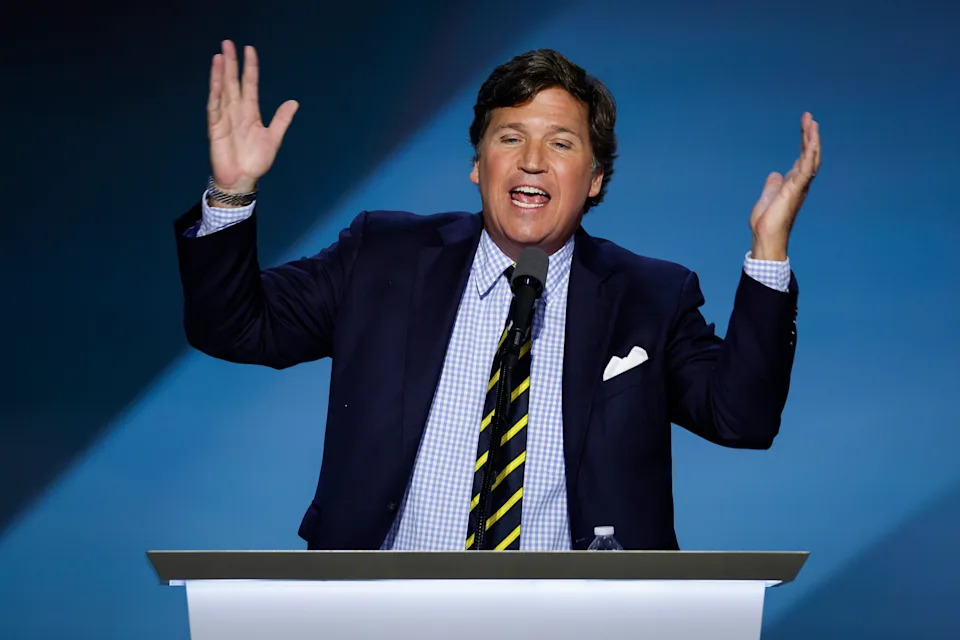 A person in a suit speaks passionately at a podium with hands raised, conveying emphasis or emotion