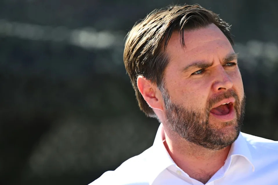 A person with short hair and a beard is speaking, wearing a collared shirt