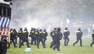 Niederländische Polizisten laufen auf eine Rasenfläche, im Hintergrund Demonstranten.