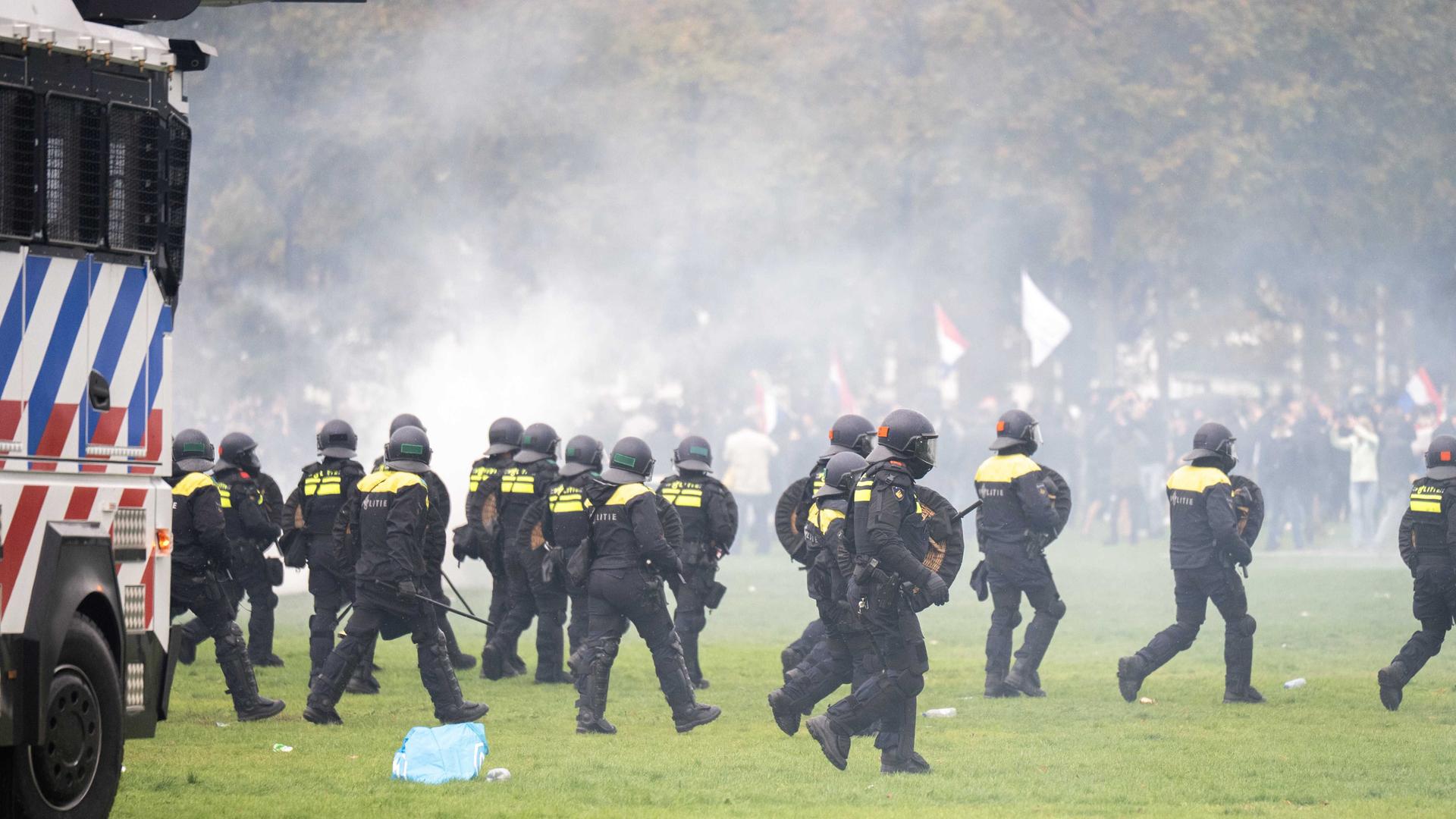 Niederländische Polizisten laufen auf eine Rasenfläche, im Hintergrund Demonstranten. Niederländische Polizisten laufen auf eine Rasenfläche, im Hintergrund Demonstranten.