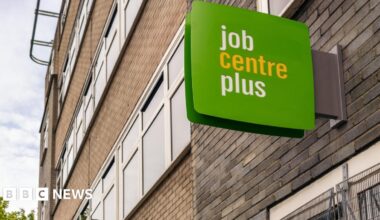 A green and white job centre plus sign on the outside of a red and grey brick modern building.