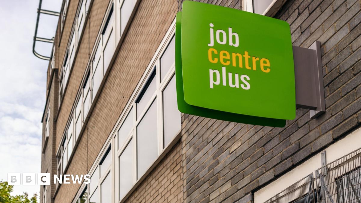 A green and white job centre plus sign on the outside of a red and grey brick modern building.