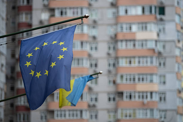 European Union and Ukrainian flags hang outside with a tall apartment building in the background.