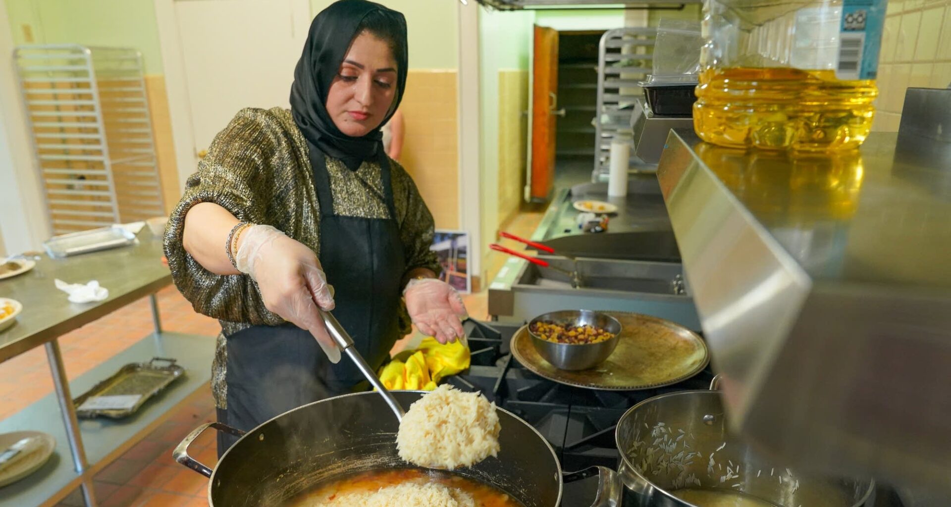Breshna Alemi ladles rice into simmering oil and onions to make Qabeli rice for a catering order. She's part of anentrepreneurship program Chef's Club, which helps refugee women start their own food businesses.