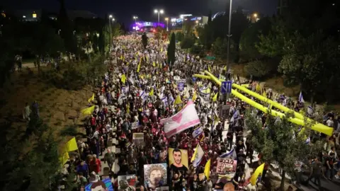 EPA A crowd of thousands holding portraits of the hostages, yellow flags and ribbons, in a Jerusalem street with trees either side 