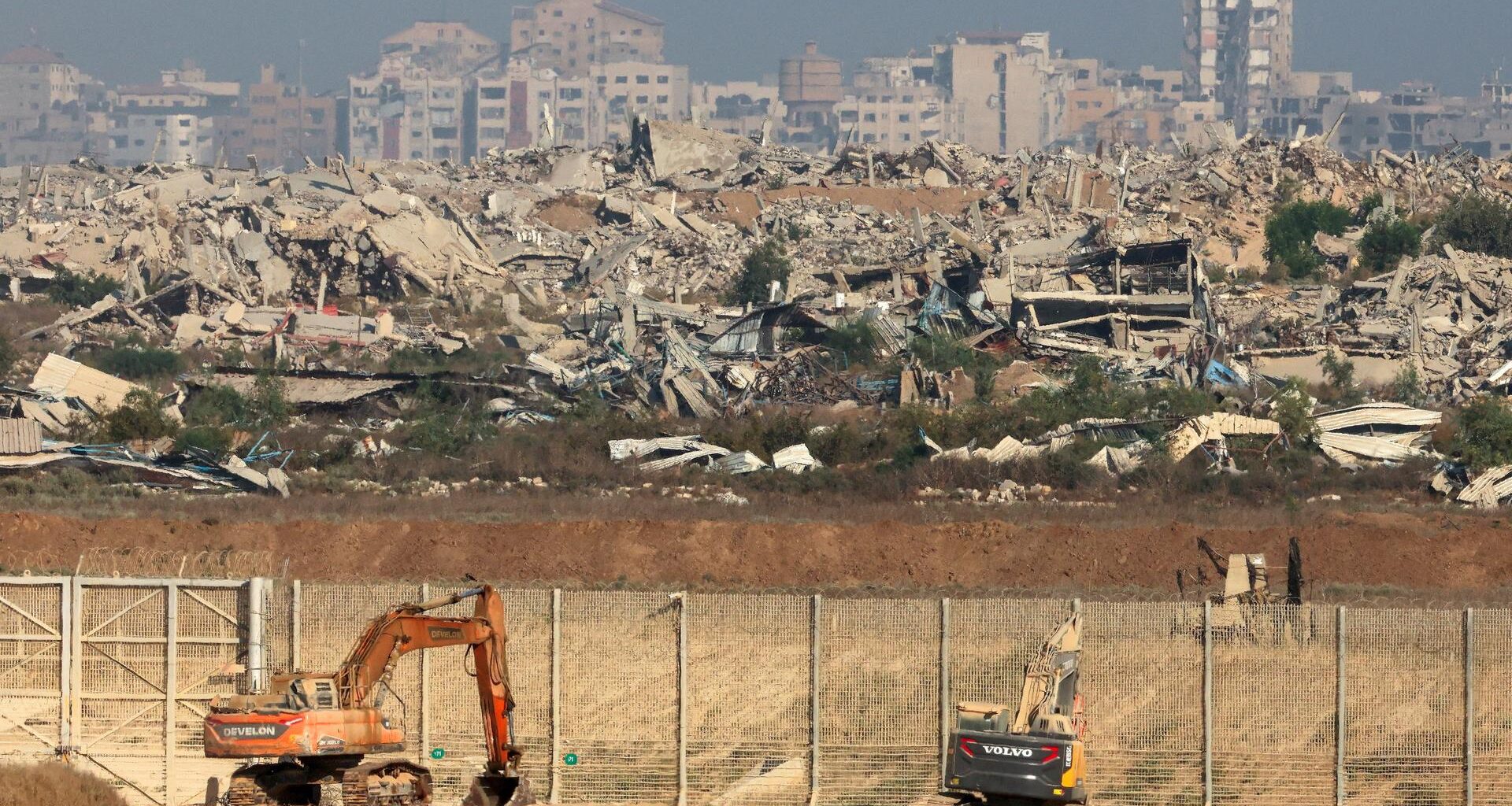 Israelische Bagger am Grenzzaun zum Gazastreifen. Im Hintergrund sind zerstörte Häuser.