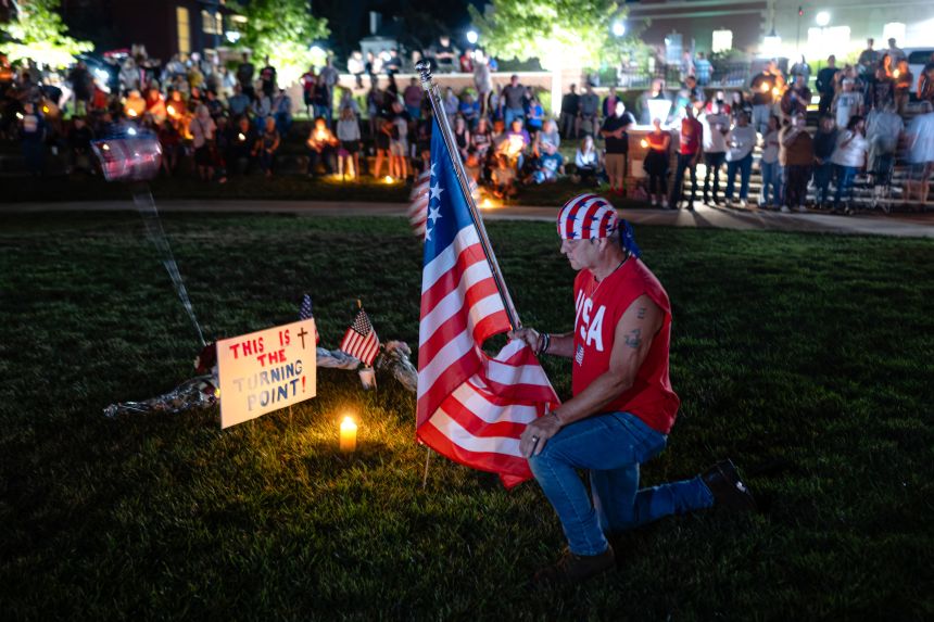A man who identifies himself as Bubba kneels with a flag during a Charlie Kirk vigil at Burlington Commons on September 17, 2025 in Burlington, Kentucky.