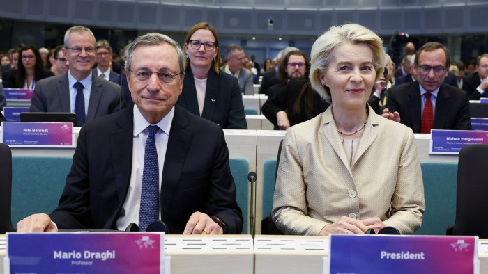 Mario Draghi and Ursula von der Leyen sit side by side at a conference table in Brussels before delivering a keynote address, with attendees in the background