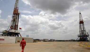 An oilfield worker in red coveralls walks near two drilling rigs at a PDVSA oil well in Venezuela’s Orinoco belt.