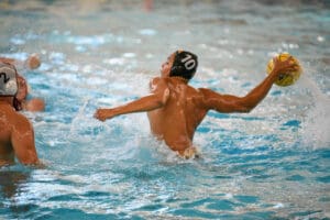 Water polo player in action, ready to throw ball in pool arena, wearing cap number 10.