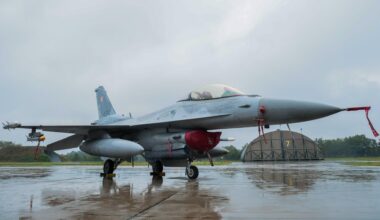 Ein Kampfjet steht auf einem Rollfeld auf der polnischen Militärbasis in Lask. Der Boden ist nass vom Regen, im Hintergrund graue Wolken.
