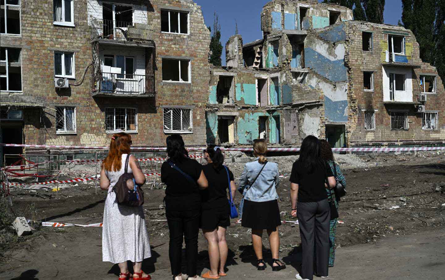 Local residents stand in front of the residential building heavily damaged three days ago during a large-scale Russian drone and missile attack, in Kyiv on August 31, 2025.