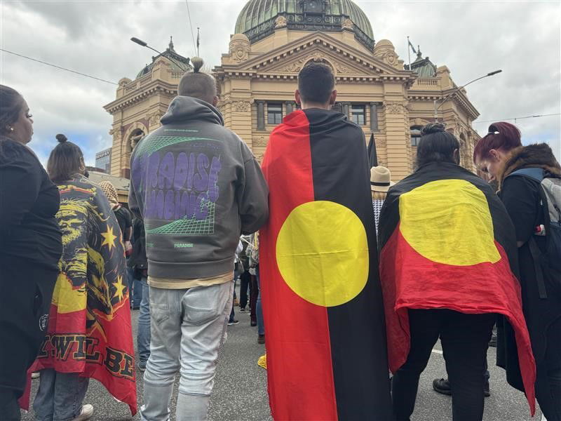 People stand around draped in aboriginal flags