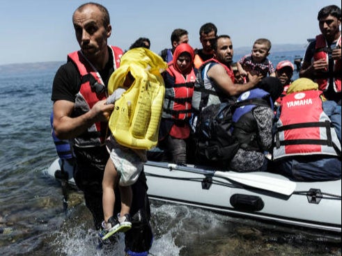 A Syrian migrant helps children get off of an inflatable boat after it arrived on the Greek island of Lesbos