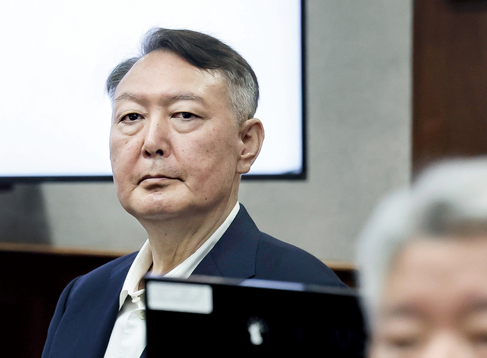 Former President Yoon Suk Yeol, who appeared in court on the 26th to contend with charges such as obstruction of the execution of special public affairs indicted by the special prosecution team for rebellion, is staring at the camera. Former President Yoon, who appeared for the first time in 85 days since his re-arrest in July, was wearing a navy suit and his short hair was white. [Joint Photography Foundation]