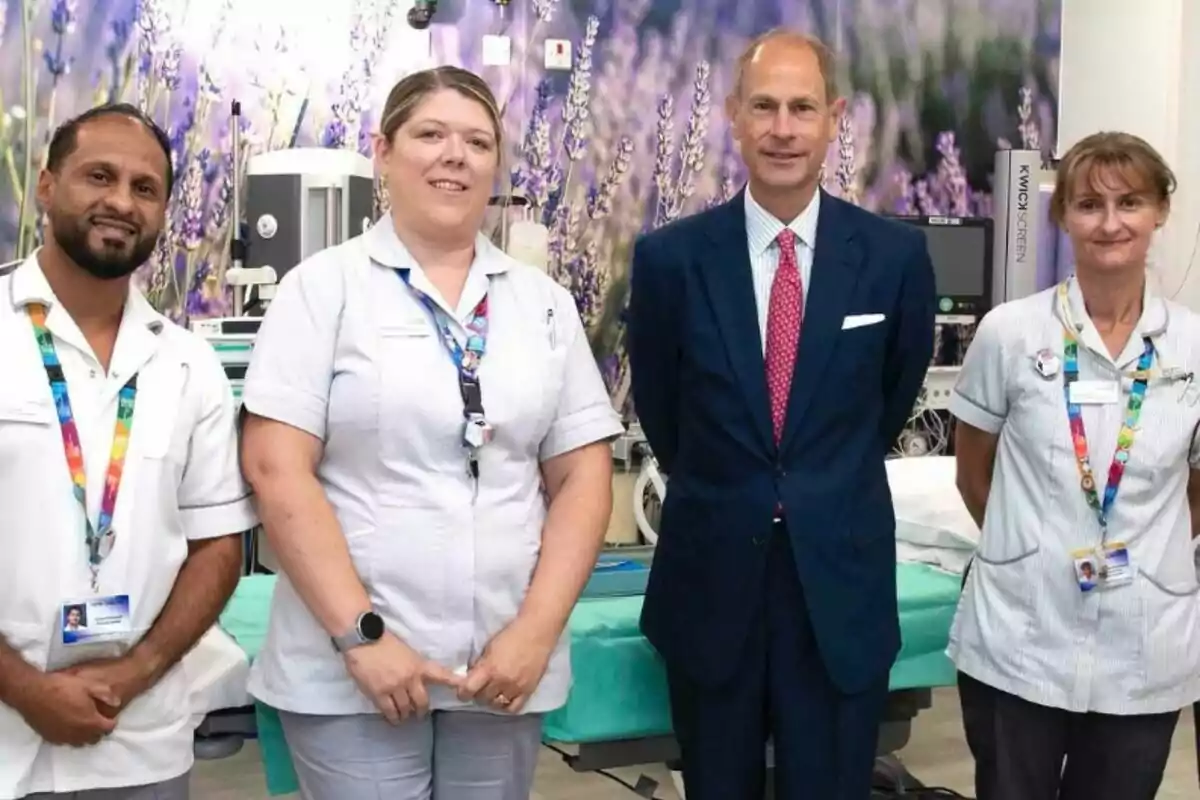 Four people pose in a hospital setting, three of them in medical uniforms and one in formal attire, with a background decorated with images of lavender.