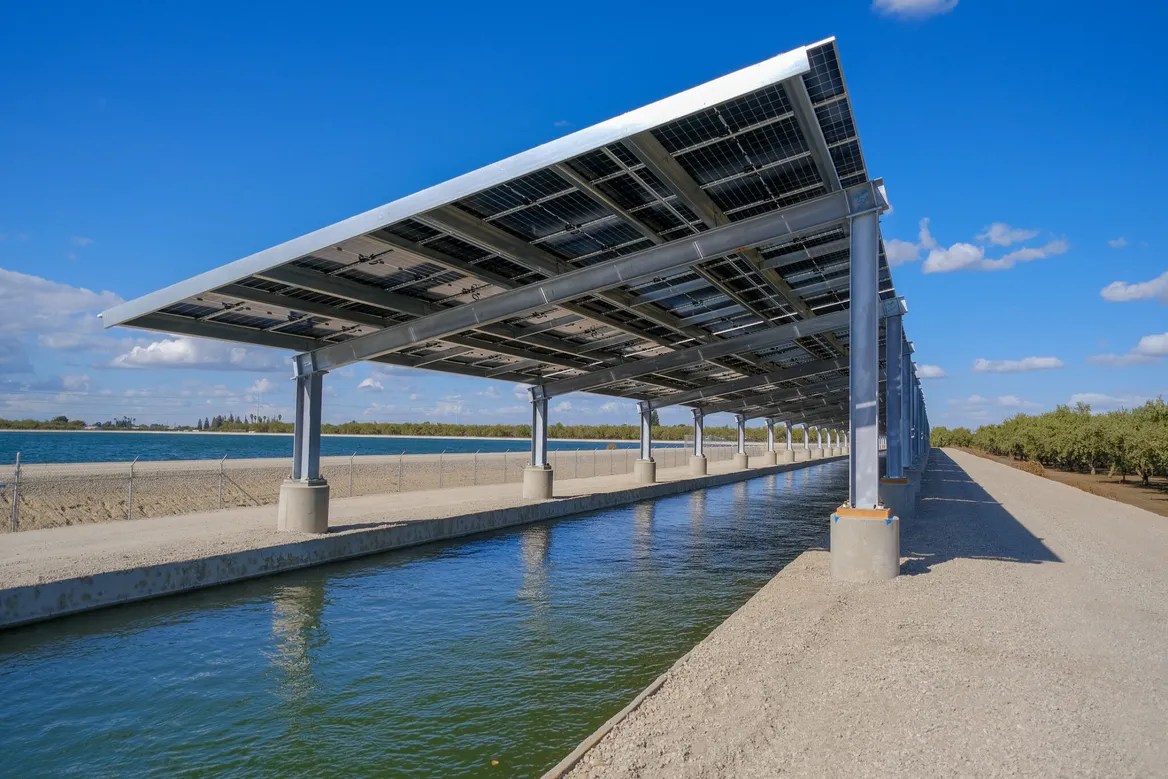 A solar panel mounted over a skinny stretch of a canal.