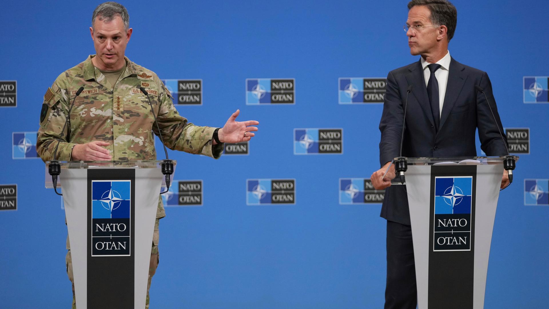 NATO-Generalsekretär Rutte und der Oberbefehlshaber der alliierten Streitkräfte in Europa, Grynkewich, stehen an Rednerpulten nebeneinander. Grynkewich, der eine Tarnuniform trägt, gestikuliert mit einer Hand.