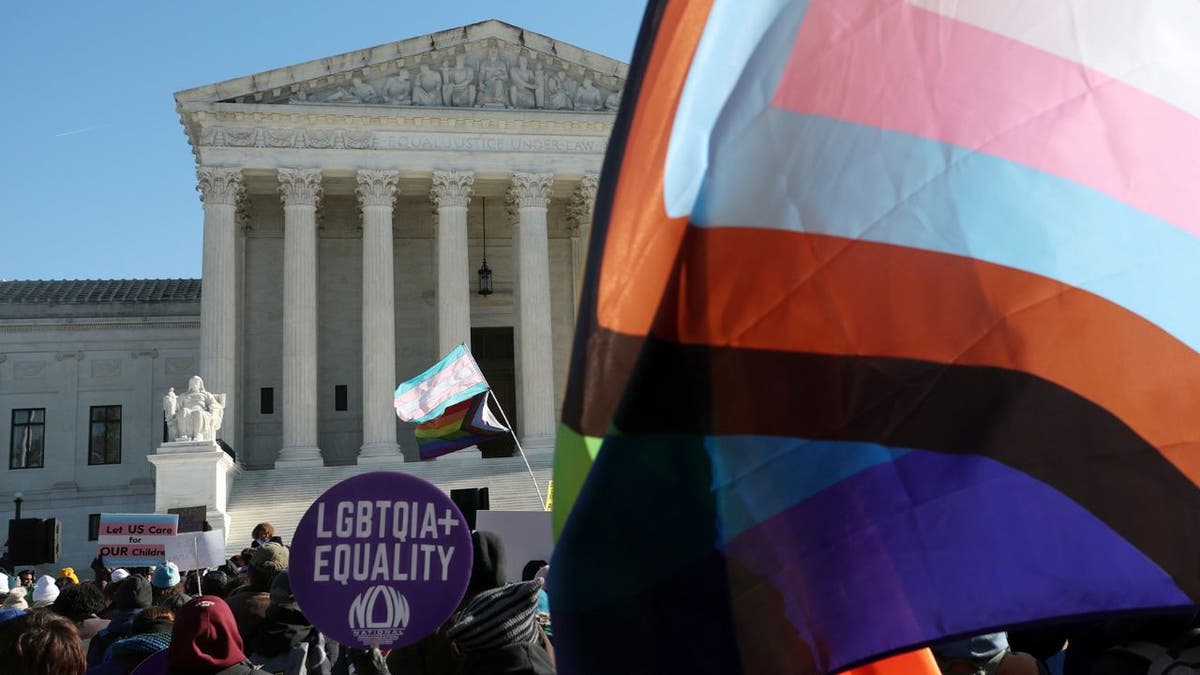 Protesters during the Skrmetti case in front of SCOTUS with the trans and LGBTQ flags.