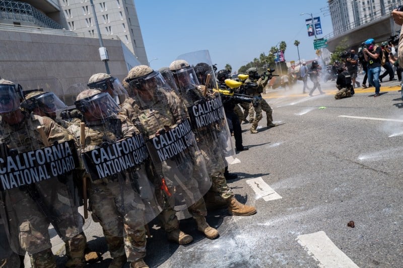 On the left are Marines in riot gear and on the right are demonstrators protesting.