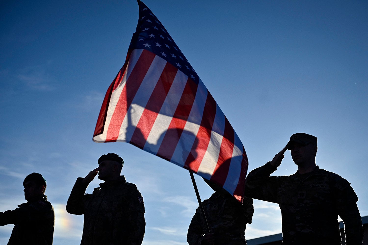 Soldiers are silhouetted as they salute under a U.S. flag.