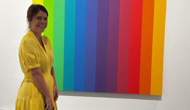 Princess Eugenie wearing a yellow dress standing in front of a rainbow painting