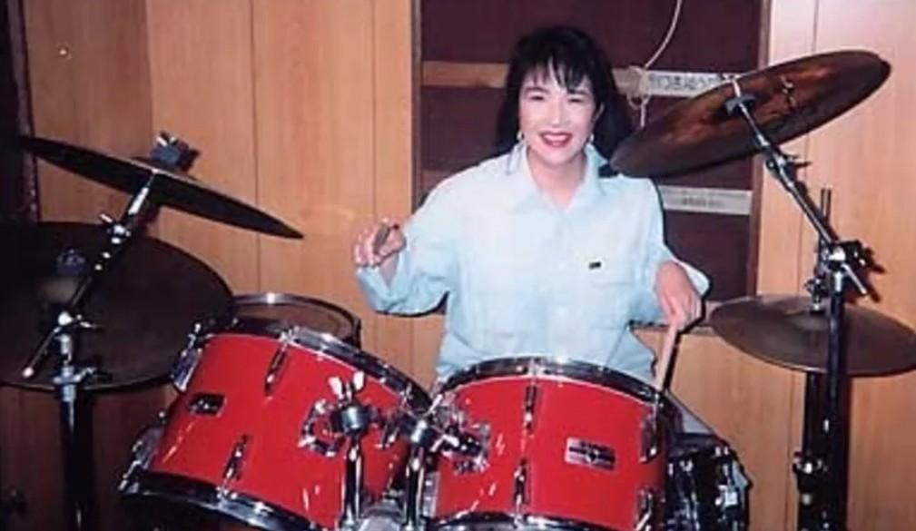 Sanae Takaichi playing red drums with drumsticks.