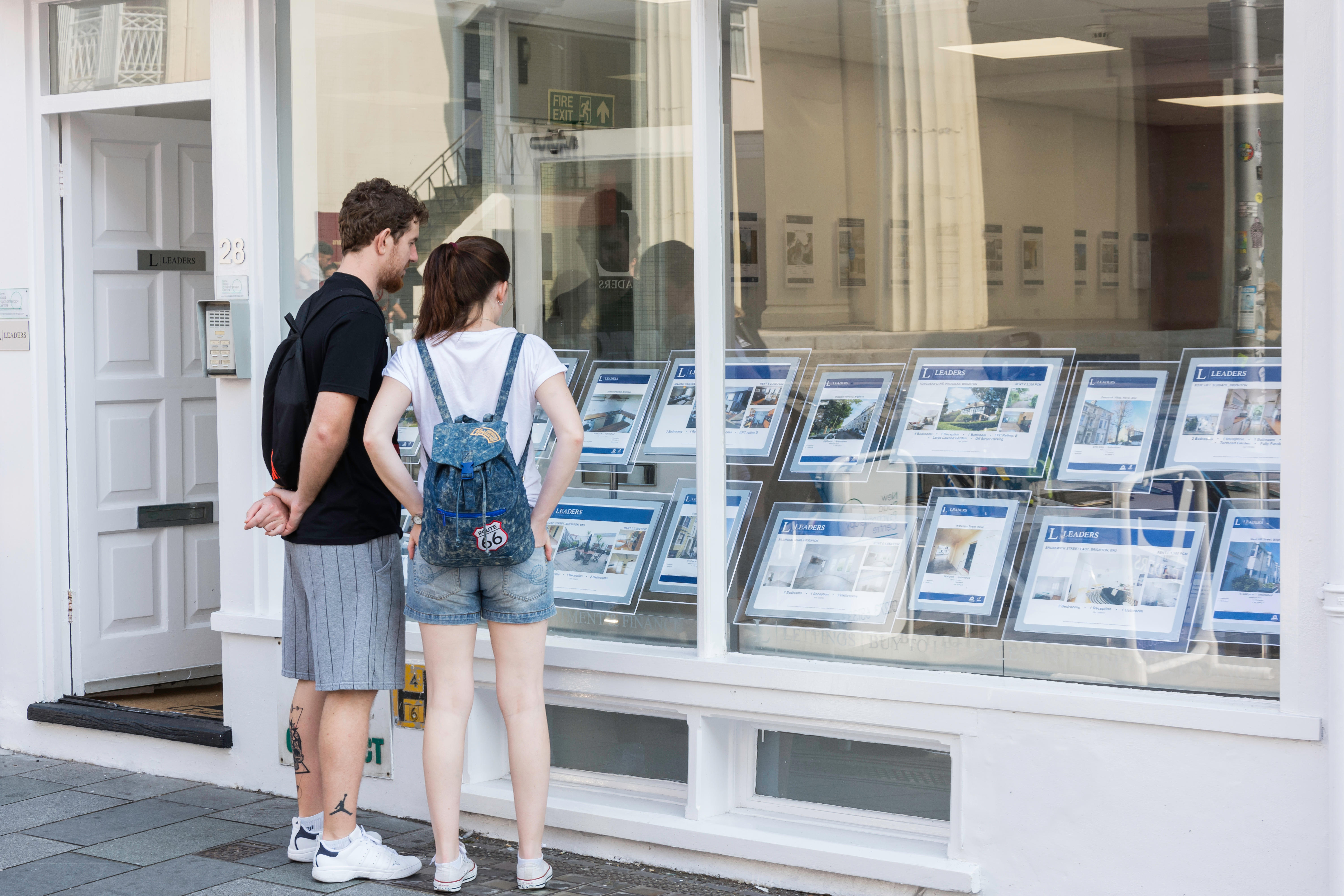 Young couple looking in an estate agent's window displaying property listings.