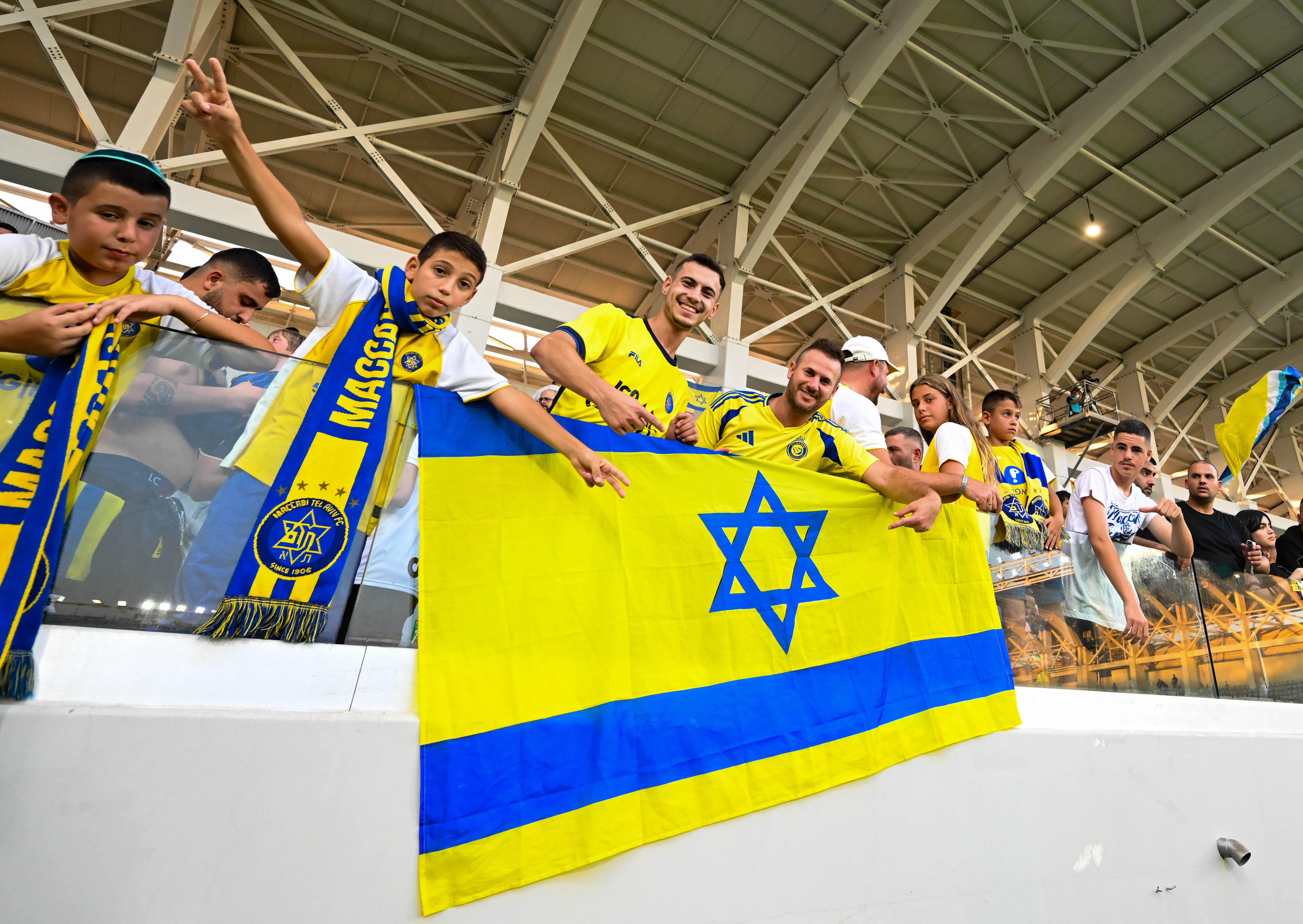 Fans of Maccabi Tel Aviv hold up team flags and scarves in the stands before a UEFA Champions League game.