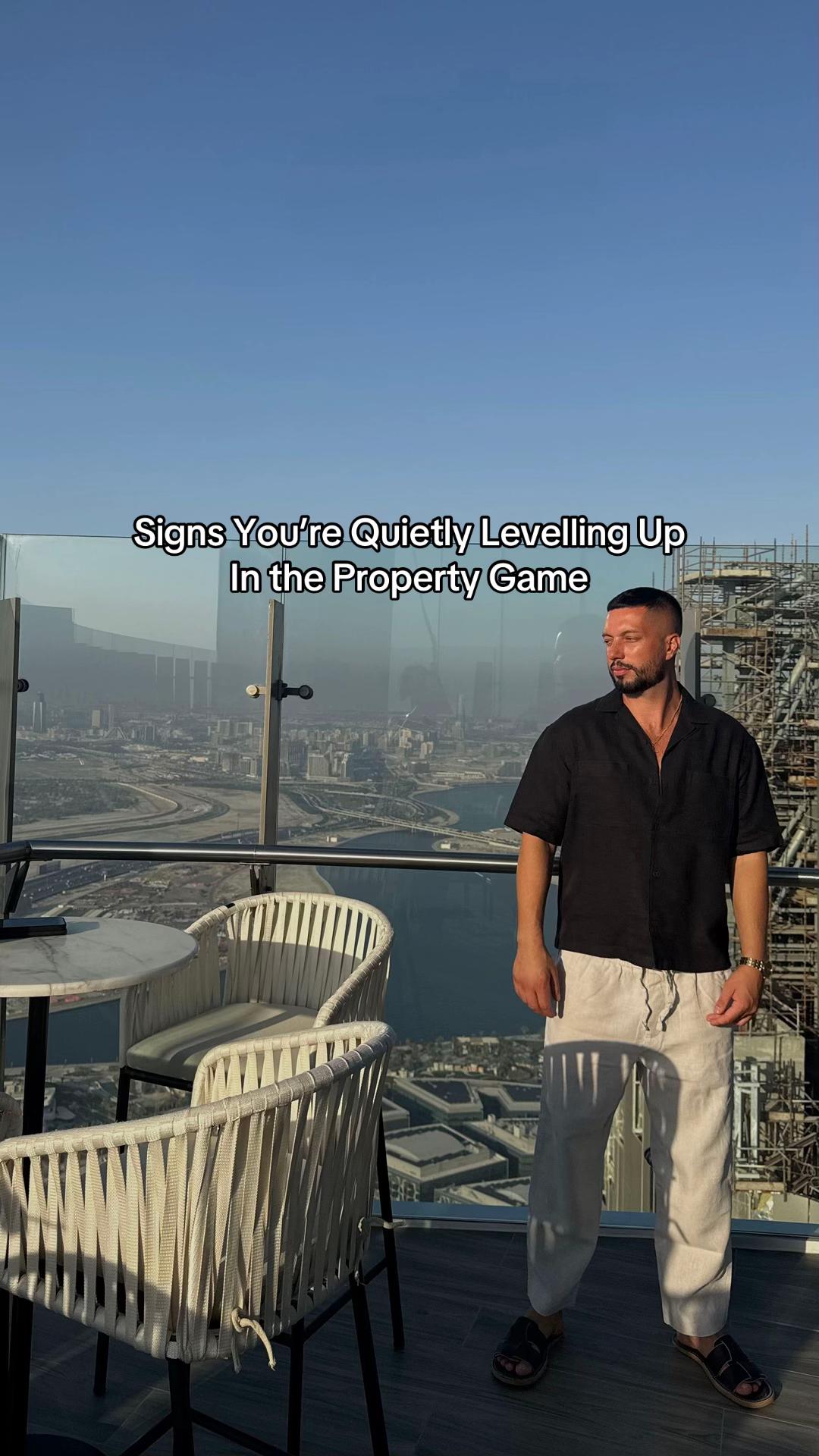 Luigi Newton on a high-rise balcony overlooking a city skyline with text "Signs You're Quietly Levelling Up In the Property Game".