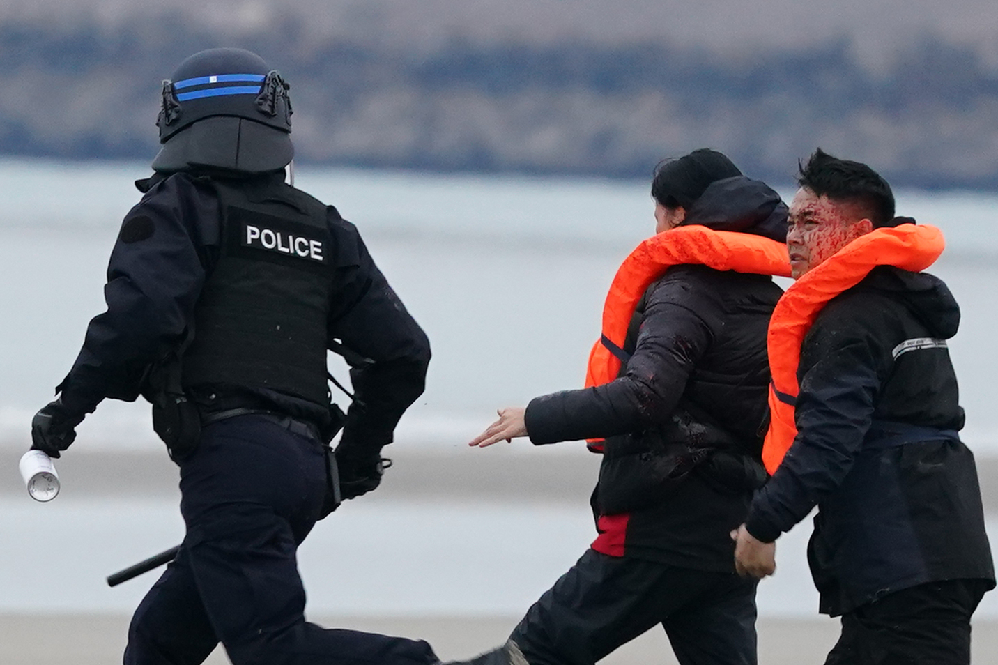 A French police officer chases and sprays people thought to be migrants on a beach in Gravelines, France.
