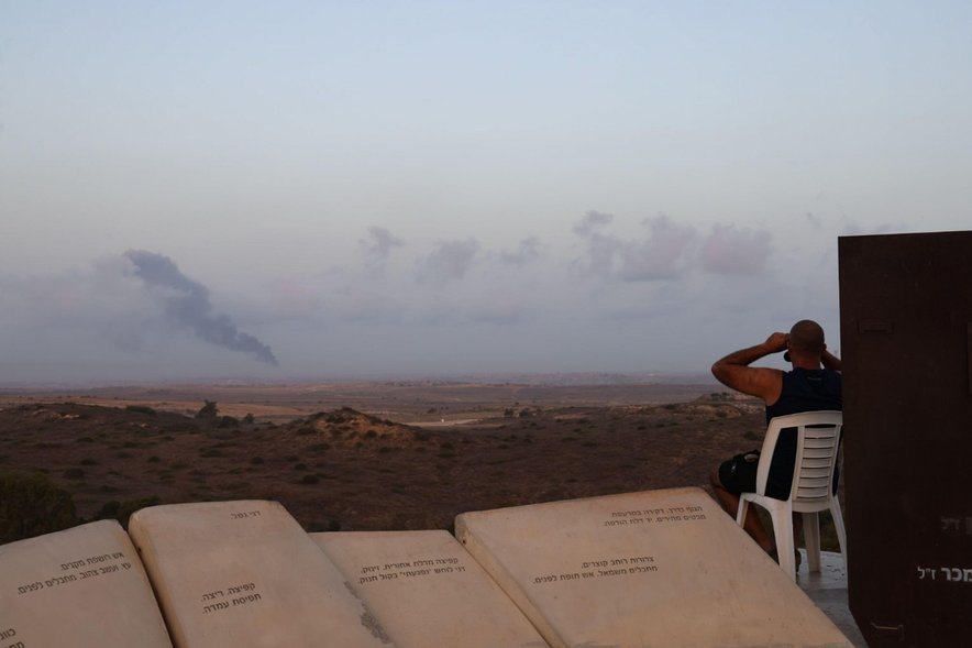 Posedanje z daljnogledom, v ozadju dim nad Gazo